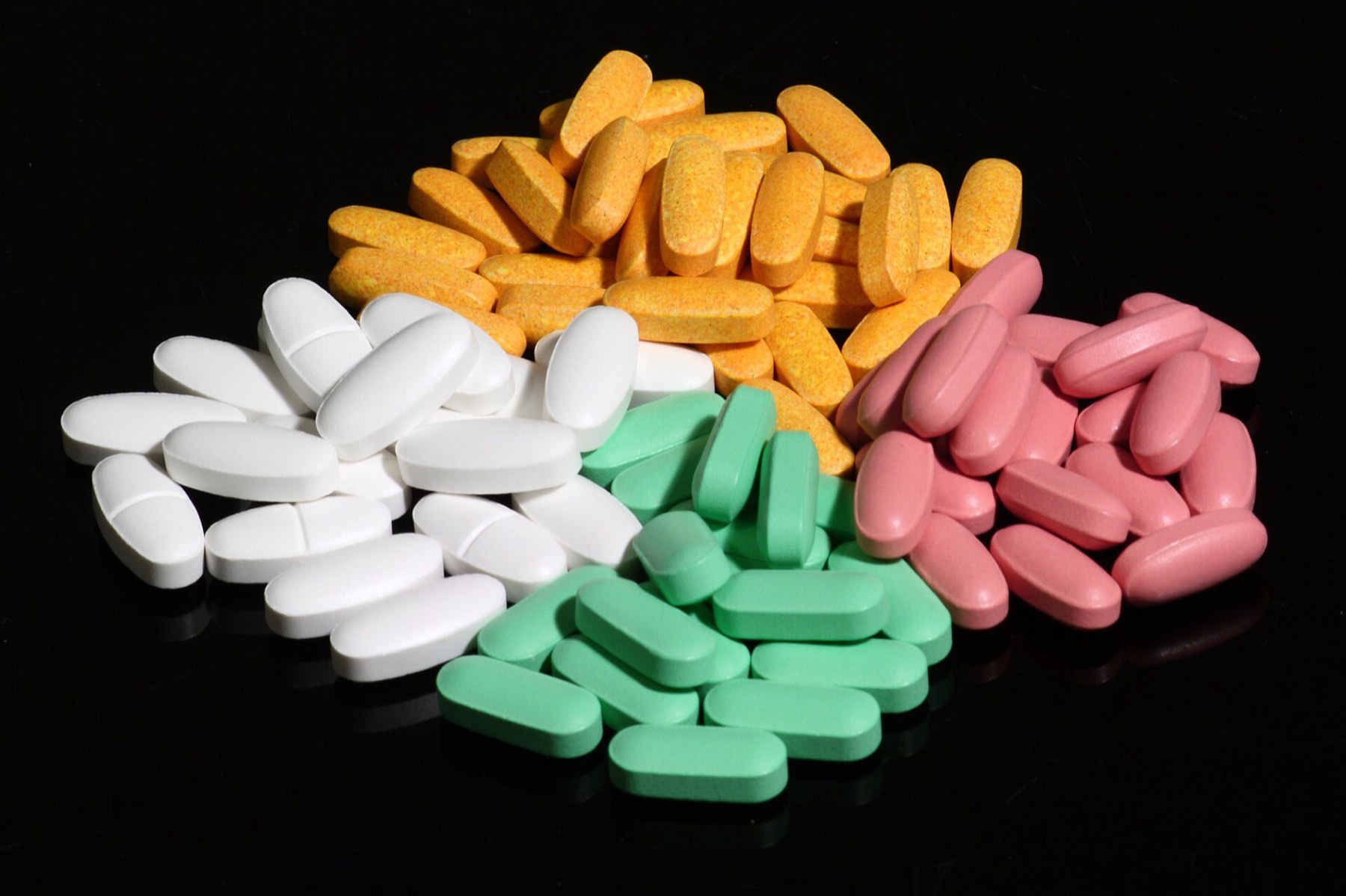 Piles of white, orange, green and pink supplement tablets on a black surface